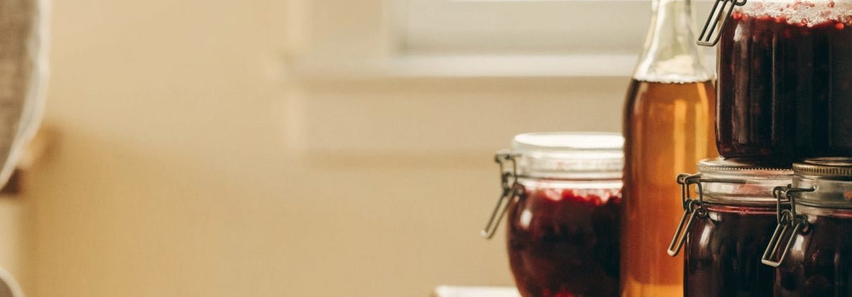 Jars of raspberry preserves and a bowl of fresh raspberries on a wooden kitchen counter